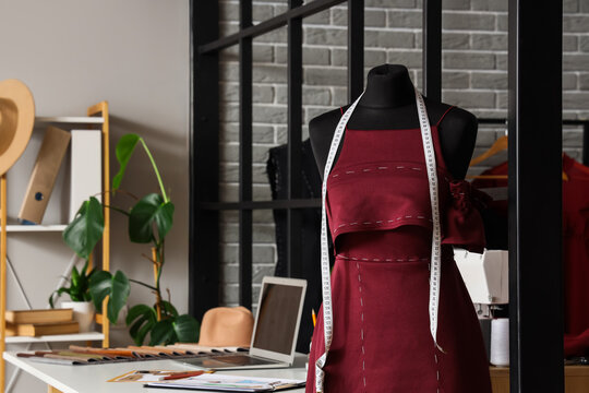 Tailors mannequin with a red dress in progress and a measuring tape in a fashion designers studio