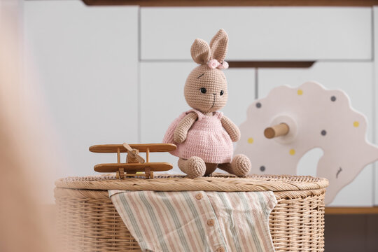 Crochet bunny doll in a pink dress with a wooden toy airplane on a wicker basket in a childs room, Childhood innocence and play, with handmade and natural elements