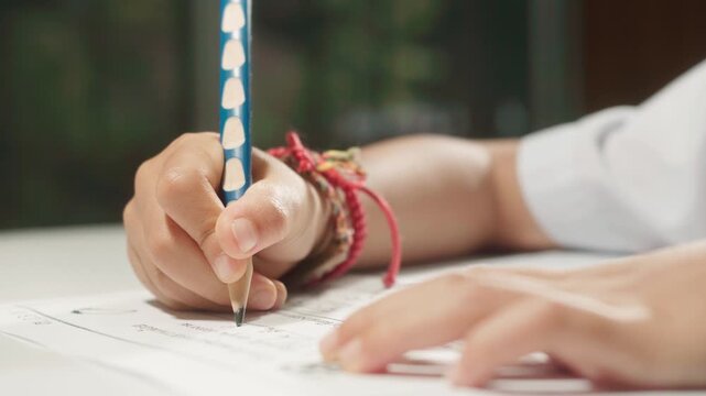 Close-up footage of a child's hand holding a pencil and practicing handwriting on a worksheet, highlighting fine motor skills, learning, education, and early childhood development.