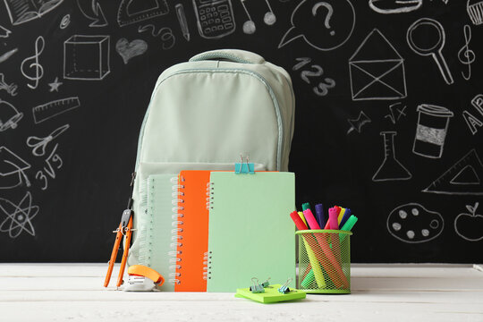 School backpack with colorful notebooks and stationery against a chalkboard with educational doodles back to school