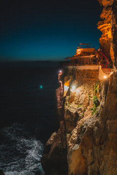 Cala en Porter, Spain - 12 May 2026: View of Cova d'en Xoroi illuminated on the cliffside overlooking the sea at night.
