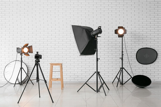 Professional photography studio setup with lighting equipment, camera on tripod, and white brick wall background