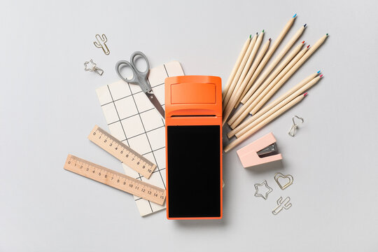 Orange payment terminal with school supplies, pencils, rulers, and scissors on a light gray background, top view