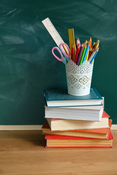 stack of books with school stationery on table against chalk blackboard. beginning of the school year, teacher's day, Knowledge Day, education, 1 september, back to school concept. template for design