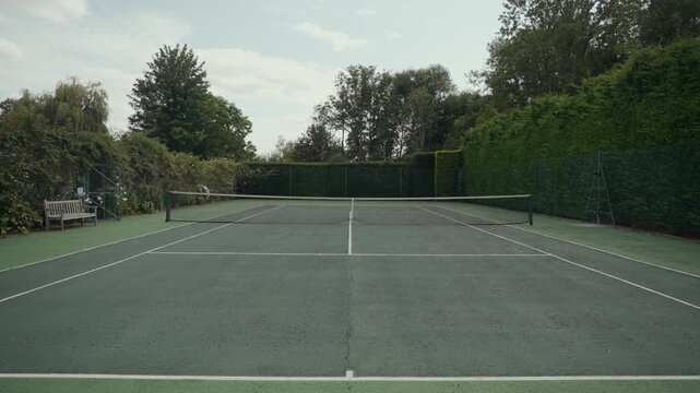 Empty green tennis court surrounded by lush foliage and a net