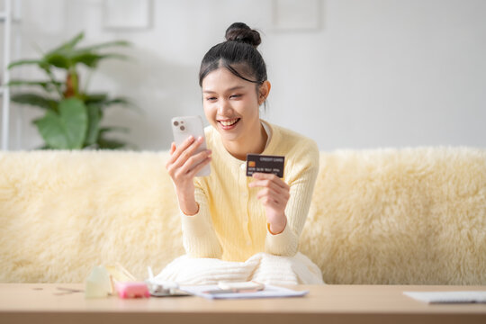 Asian woman using smartphone with credit card at home, online travel insurance purchase, vacation payment, travel expenses, trip booking, financial protection concept.