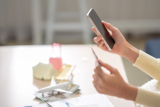 Close up woman using smartphone with credit card beside airplane, cash, suitcase, travel insurance documents, online payment, vacation expenses, trip protection concept.