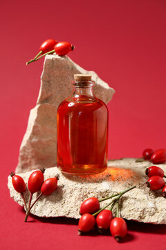 Stones with bottle of cosmetic rose hip oil and berries on red background