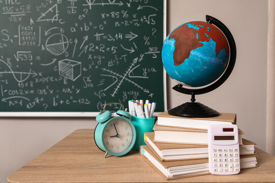 Globe with books, pen cup and alarm clock on desk in classroom