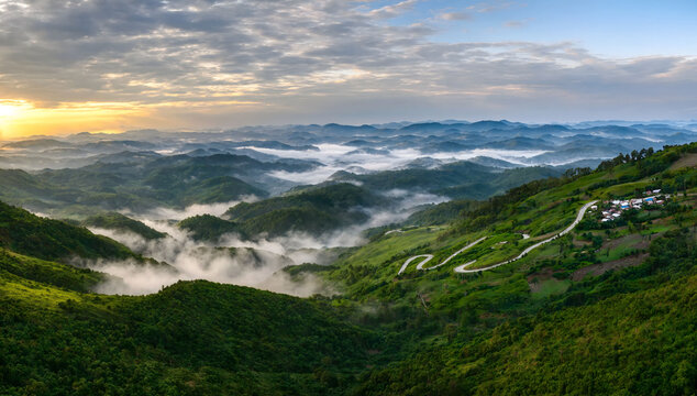 Misty green mountain valley with winding road under soft sunset sky in Bandarban