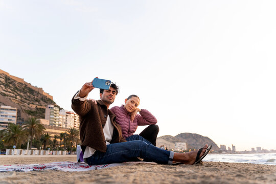 Couple on winter beach taking selfie with smartphone, enjoying coastal travel