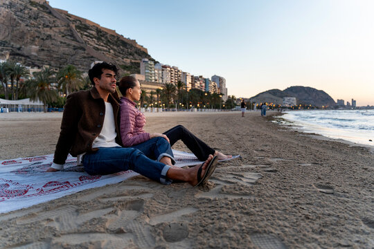 Couple relaxing on beach watching sunset during winter travel in alicante