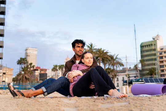 Couple relaxing on beach during winter with city skyline background