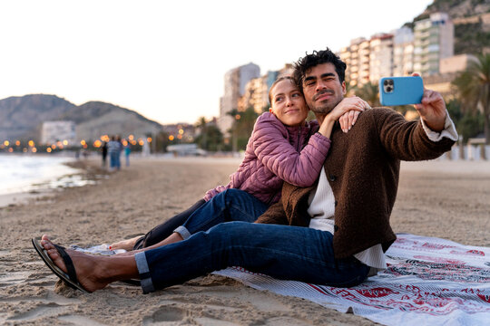 Happy couple on winter beach, capturing selfie moments at golden hour