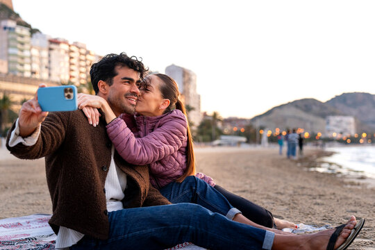 Couple taking selfie on beach during winter vacation at sunset