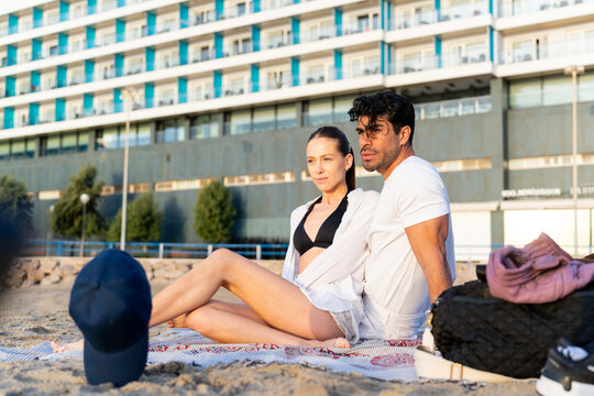 Couple relaxing on beach towel near hotel, enjoying a sunny winter day