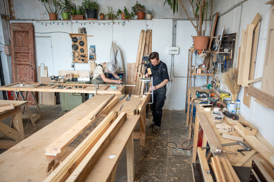 Men at work, qualified focused carpenters working at restoration workshop on wooden furniture repair, craftsmen using electric machinery and hand tools at workstations, small business repair studio.