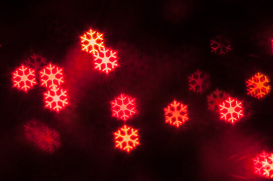 Glowing red snowflake shaped bokeh lights softly blurred on a black background, suitable for Christmas and New Year design projects