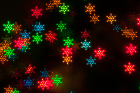 Multicolored snowflake bokeh lights glowing on black background. Festive winter Christmas and New Year holiday texture showing colorful red, green, and blue snowflake shaped lights