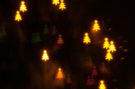 Warm yellow christmas tree bokeh lights - minimalist holiday background featuring bright golden Christmas tree shaped bokeh lights shining in the dark