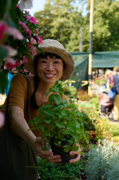 Smiling Woman in Straw Hat Holding a Potted Plant at an Outdoor Garden Center Market