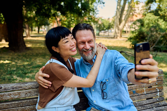 Happy Couple Taking a Selfie on a Bench in a Sunny Urban Park Showing Affection