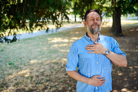 Middle-Aged Man Practicing Mindful Breathing and Relaxation in a Sunny Park Under Trees