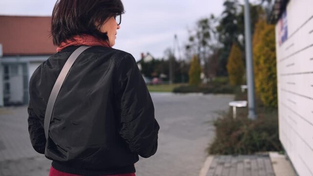 Woman Walking To Parcel Locker To Pick Up Package With Smartphone In Hands On Parking