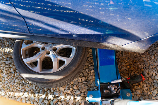 Blue car on rolling jack and wheels lying under car for safety