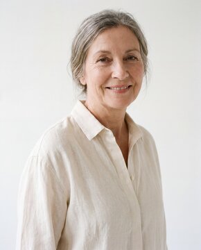 Smiling woman with gray hair in cream button down shirt against a plain white studio background