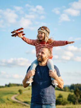 Father carries child with toy airplane on shoulders outdoors
