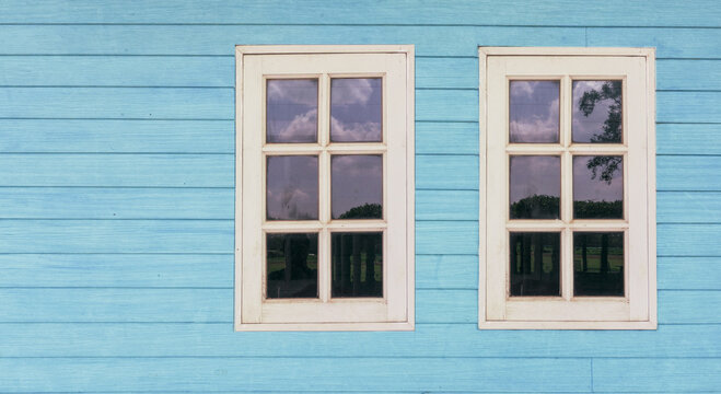 two old white windows on teal blue wood wooden wall , rustic vintage rural house home background , nostalgia concept 