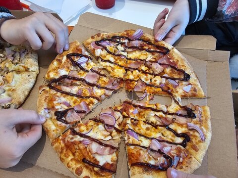 Pizza is shared among friends at a table in a casual dining setting with hands reaching for slices concept
