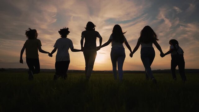 Large family running forward across summer field. Dark group silhouette moves against sunset sky. Happy family enjoys calm nature togetherness. Swift running group shares beautiful warm sunset.