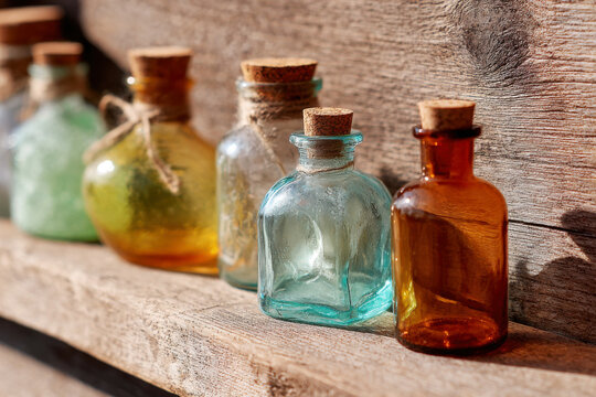 Colorful vintage glass bottles with cork stoppers lined up on a sunlit weathered wooden shelf