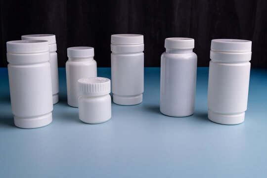 White supplement containers arranged on a light blue table surface over a black background, pharmaceutical medical concept layout