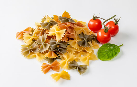 A vibrant assortment of colorful farfalle pasta served with fresh cherry tomatoes and a basil leaf on a clean white background. 