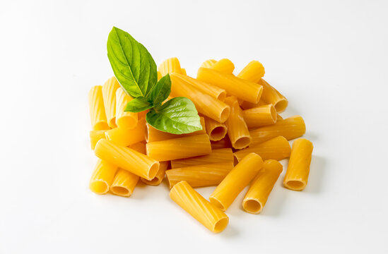 Uncooked rigatoni pasta arranged with fresh basil leaves on a clean white background. The simple composition highlights Italian cuisine, pasta ingredients, freshness, and natural food styling. 