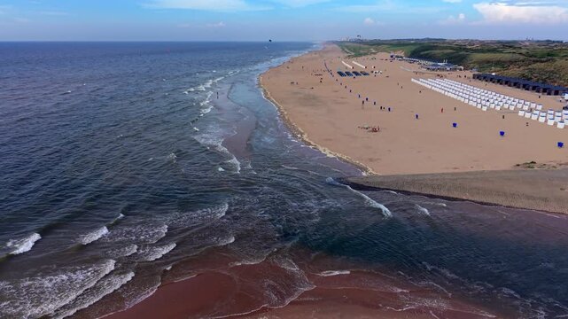 Aerial view video clip of Katwijk aan Zee river mouth Oude Rijn outlet meeting North Sea waves, beach resort, beach cabins beach houses sand dunes and Scheveningen skyline in South Holland Netherlands