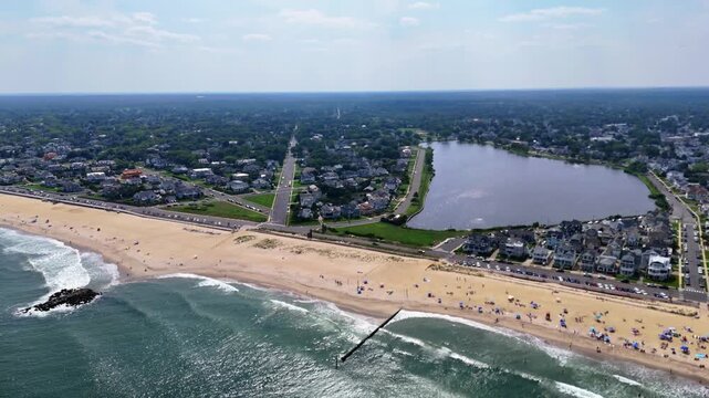 Wide aerial view of sunny Belmar Beach, ocean waves, town and lake Como in New Jersey