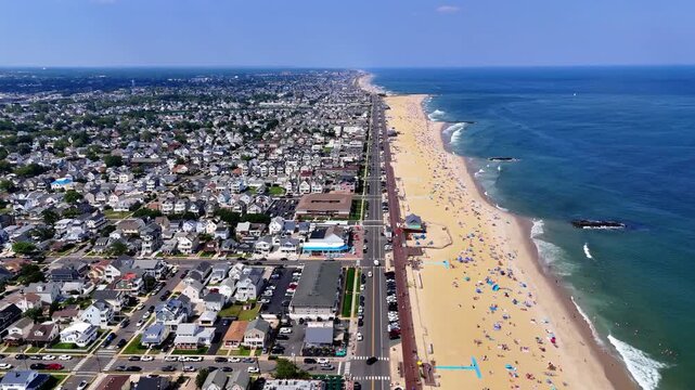 Aerial wide shot of a crowded Belmar beach with people enjoying the sunny day , houses and traffic