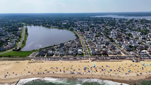 Aerial wide shot of a crowded Belmar Beach, New Jersey, town and lake Como on a clear sunny day