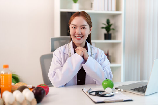 Smiling Asian female nutrition consultant sitting at desk in modern office