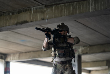 Fototapeta premium Portrait of male military soldier standing inside building wearing camouflage tactical uniform helmet with weapon for urban combat mission