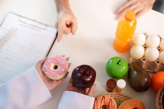 Top view of nutrition consultant showing apple and donut options to patient on desk