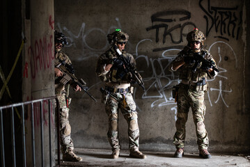 Fototapeta premium Group of armed special force soldier standing inside concrete building holding assault rifle wearing camouflage tactical uniform helmet gear for urban mission