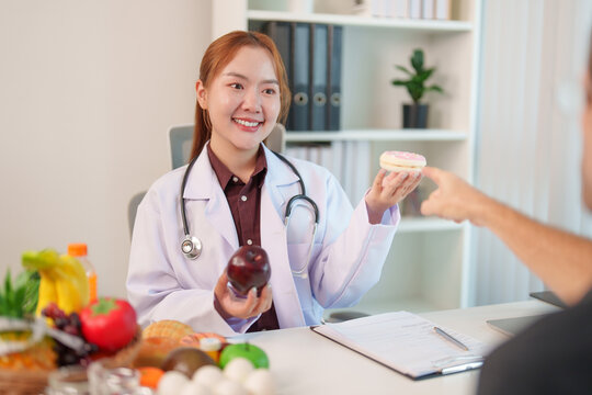 Asian nutrition consultant holding apple and donut during patient consultation in clinic