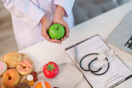 High angle view of nutrition consultant holding green apple over stethoscope and health summary
