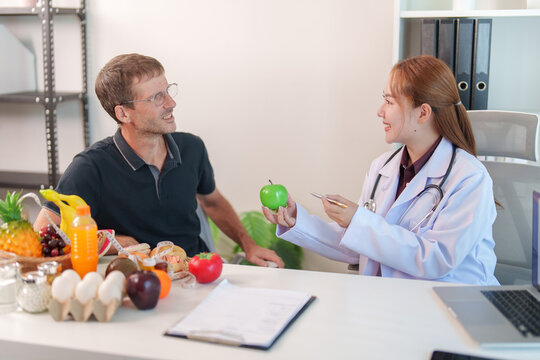 Female nutrition consultant giving dietary advice with green apple to male patient in office