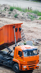 Orange dump truck with raised bed on construction site, a view from above, showing heavy machinery at work, conveying industrial development and material movement, vertical photo © HENADZY